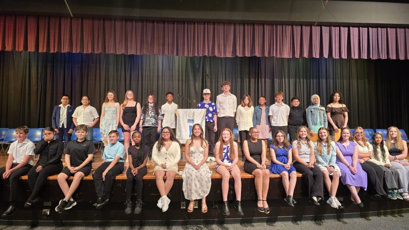 the students who were inducted into the National Junior Honor Society are seated on stage, posing for the camera.