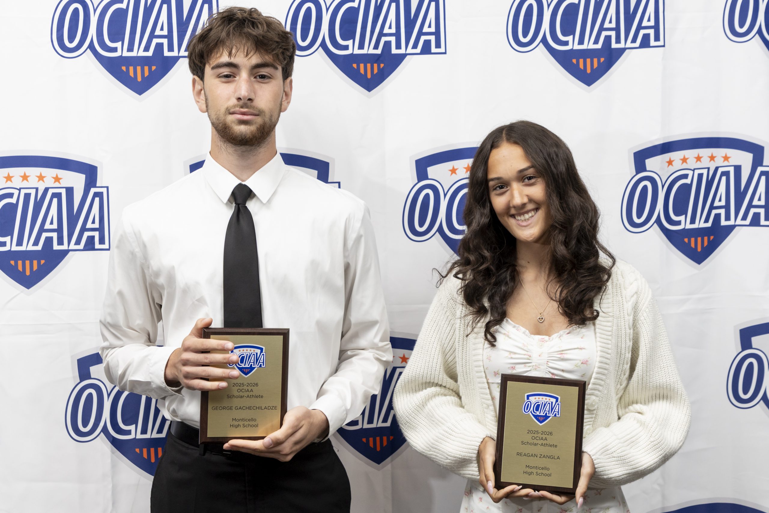 Reagan Zangla and George Gachechiladz hold their awards while posing for the camera in front of an OCIAA backdrop 