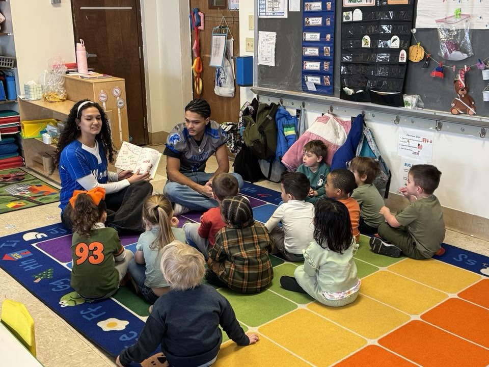 two senior athletes read to a group of students 
