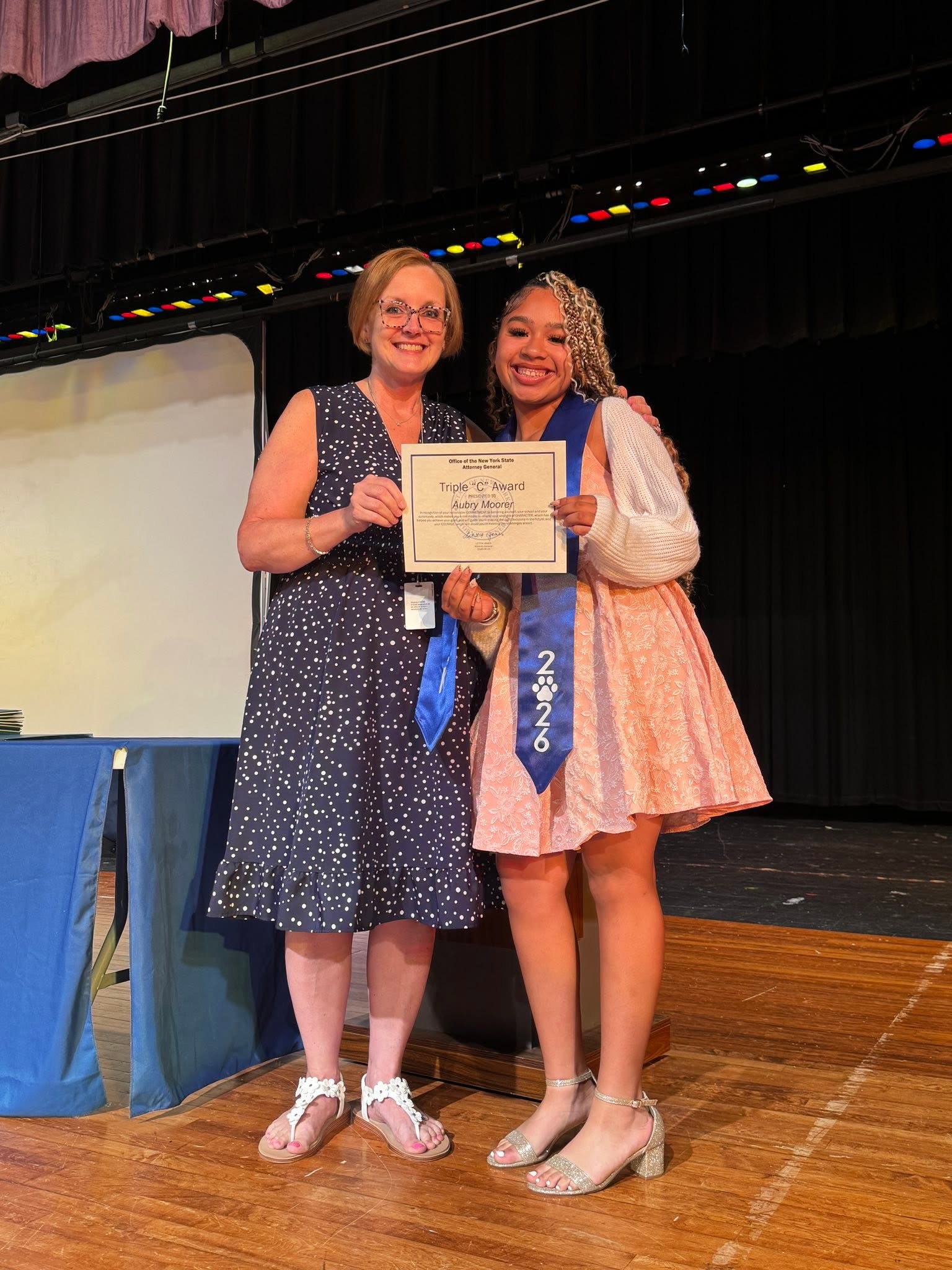 The principal poses with the recipient of the triple c award on stage