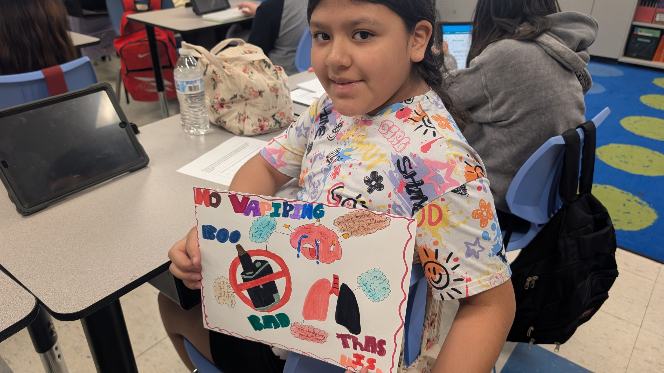 a student is holding the anti-smoking artwork she drew towards the camera
