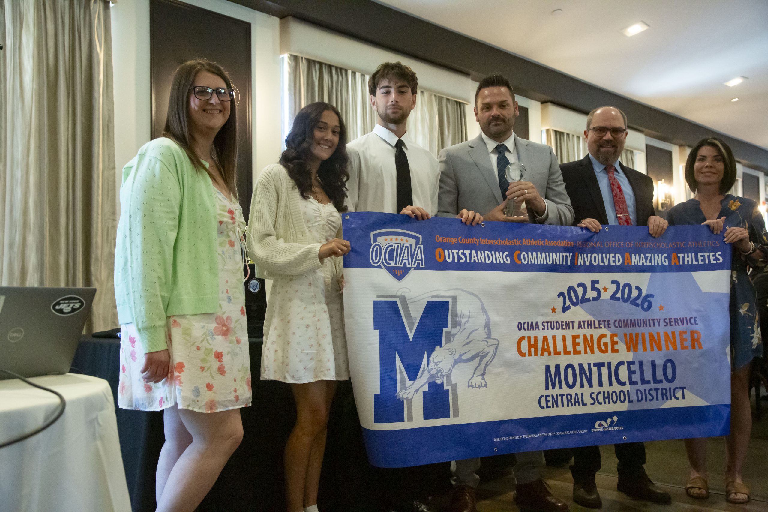 Members of Monticello's athletics department and administration pose with a banner announcing the award 