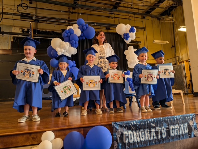 a group of graduates from the Tiny Town program pose on stage in graduation outfits