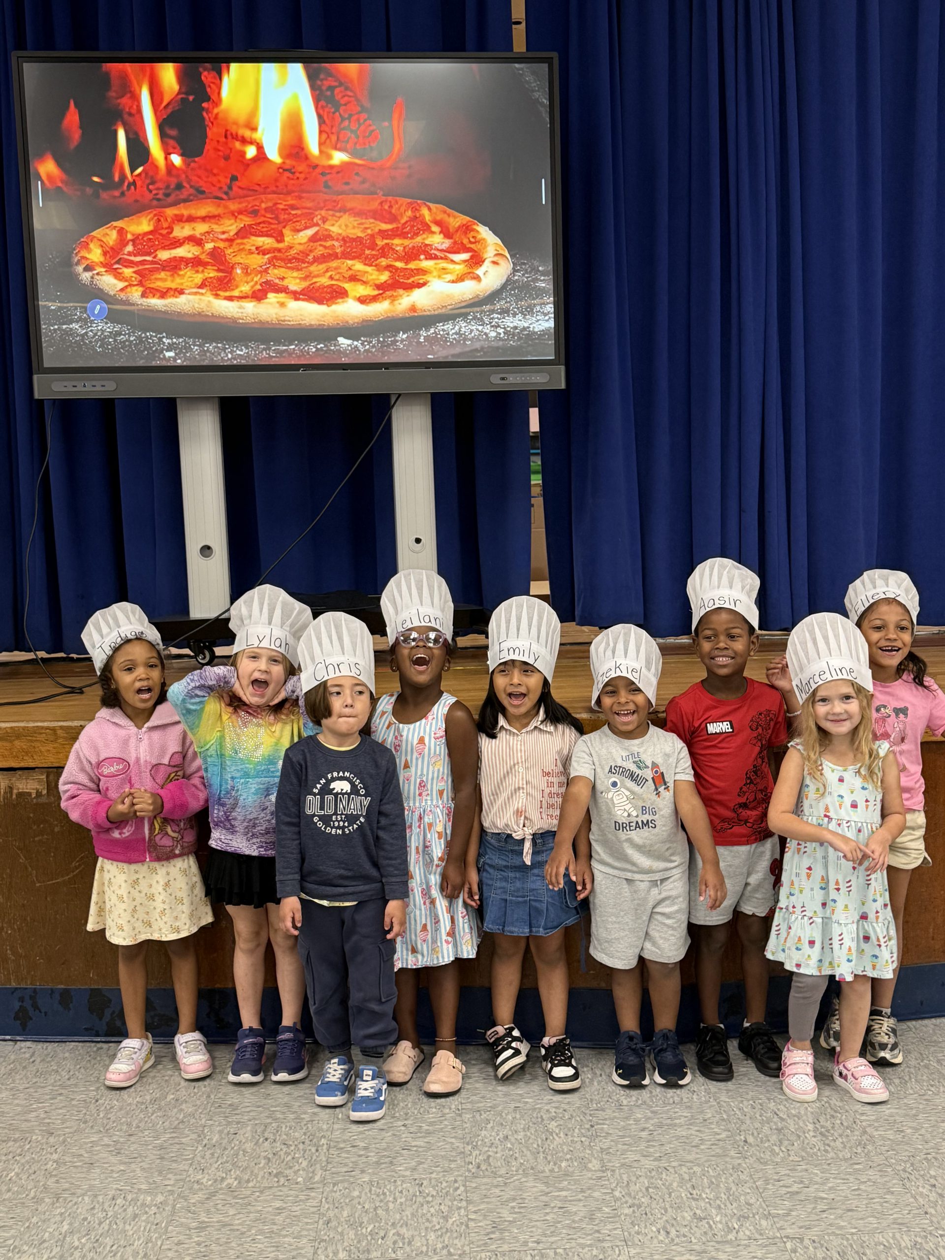a group of small children wearing chef hats are posing in front of a photo of pizza