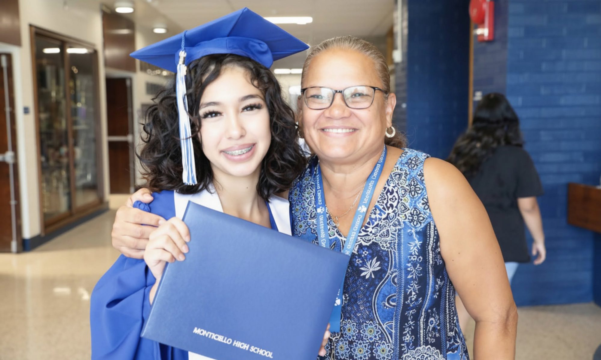 a student in graduation robes poses with a teacher