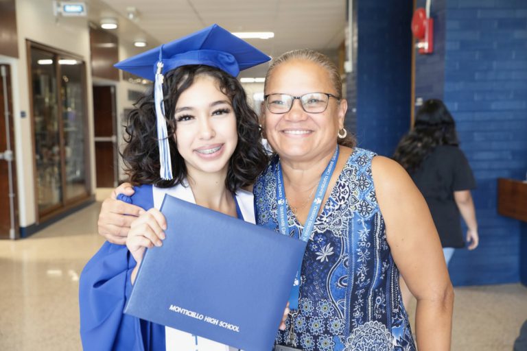 a student in graduation robes poses with a teacher